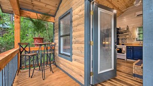 A wooden deck with a table and chairs, a kitchen with blue cabinets, and a door leading to the interior. - Romantic Broken Bow Cabin w/ Jacuzzi & Fire Pit! (Broken Bow)