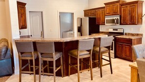 Una cocina con armarios de madera, una isla grande con taburetes de bar, un refrigerador y un microondas.