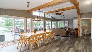 A spacious kitchen with wooden beams, a dining area with a large table and chairs, and a view of the outdoors through large windows.