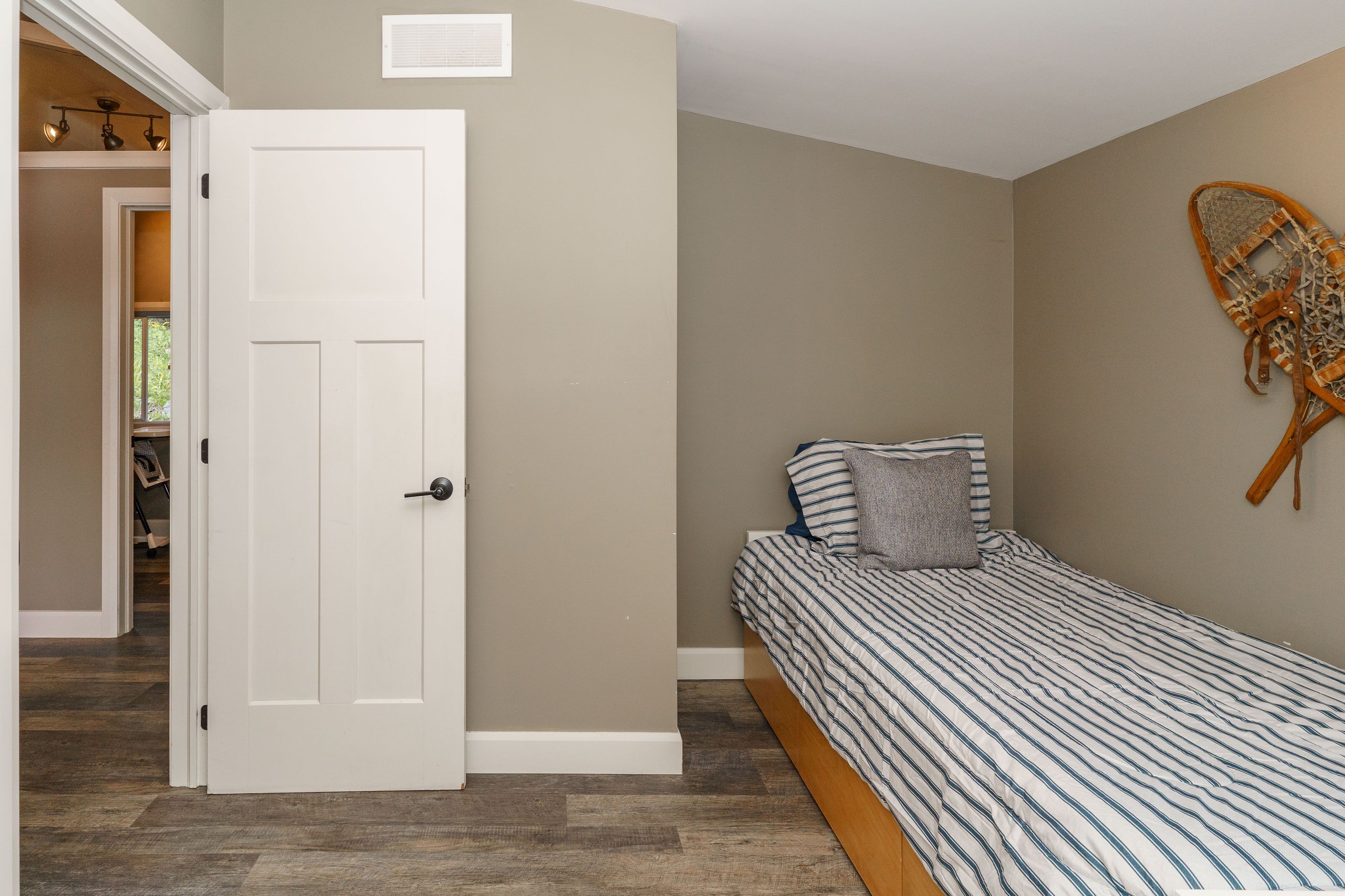 A bedroom with a bed, a door, and a wall-mounted chair.