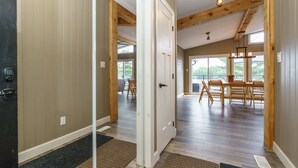 A spacious dining area with wooden chairs and a table, a door leading to another room, and a view of the outdoors through large windows.