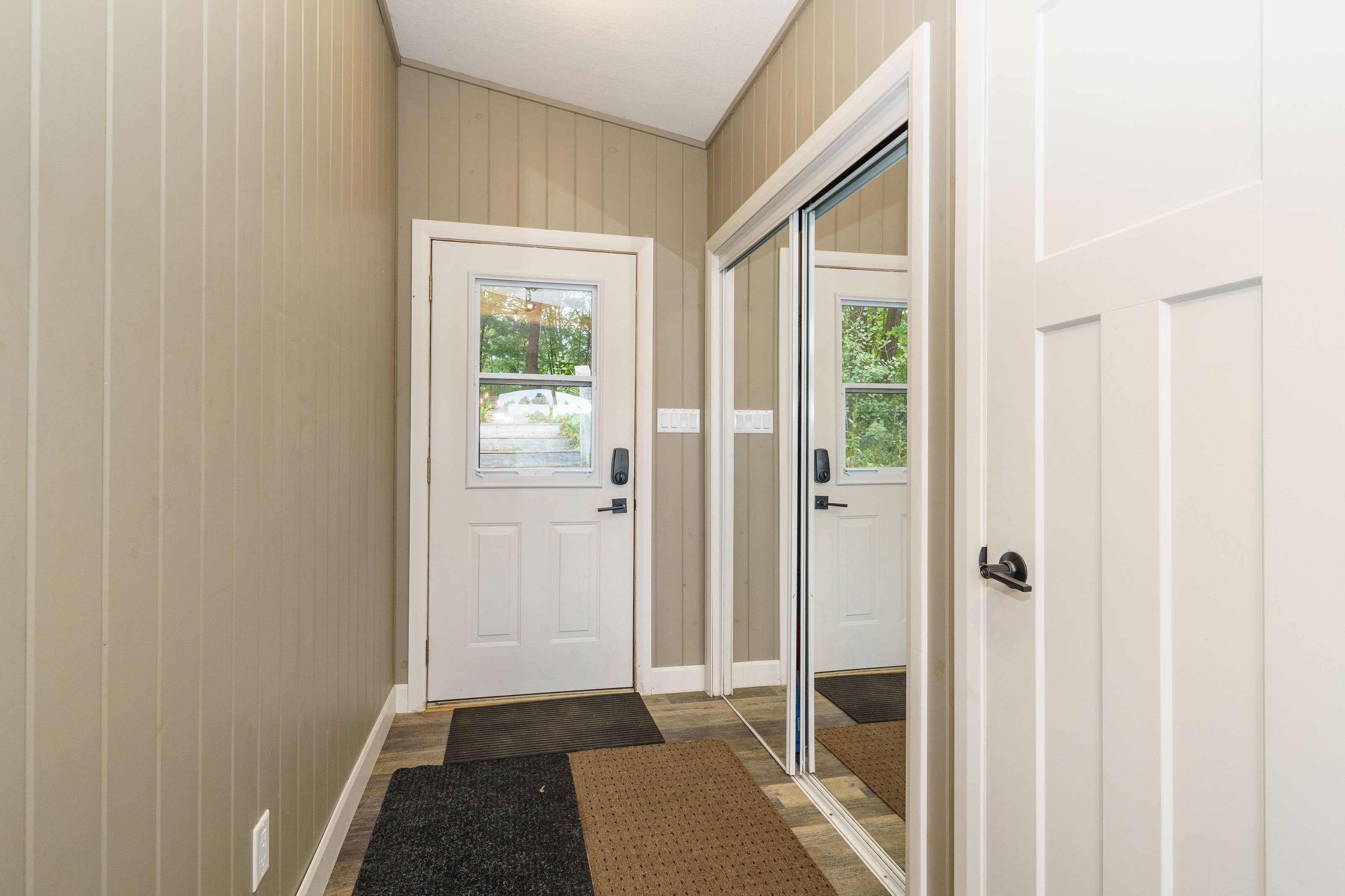 A hallway with a white door, a sliding glass door, and a doormat.