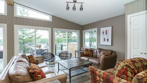 A spacious living room with a large window, a sofa, a coffee table, and a patterned armchair.