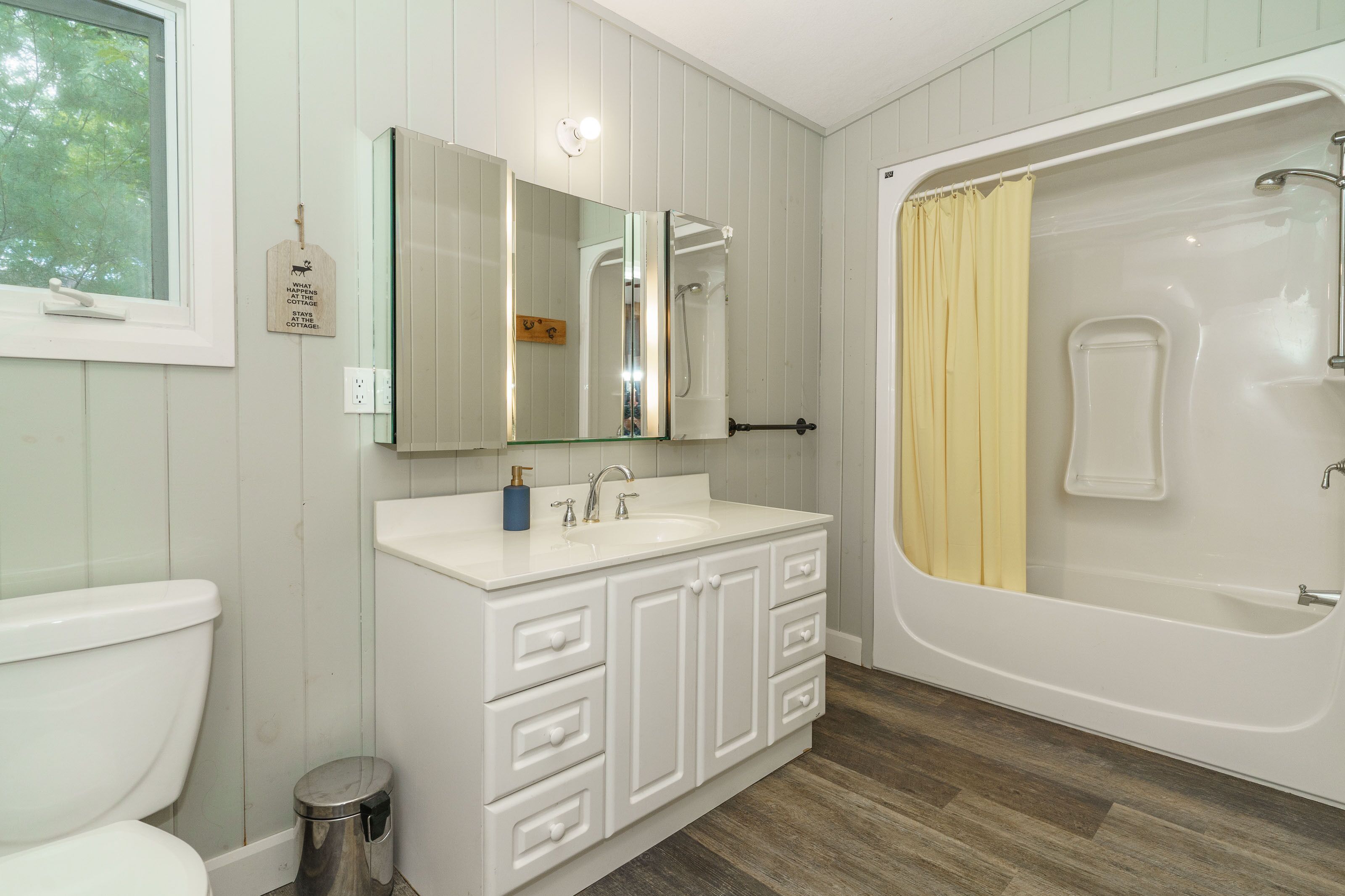 Une salle de bain avec un meuble-lavabo blanc, un miroir, des toilettes et une baignoire agrémentée d’un rideau de douche jaune.