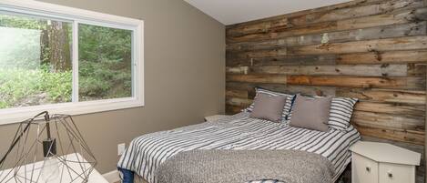 A bedroom with a bed, a nightstand, a lamp, and a window with a view of greenery.