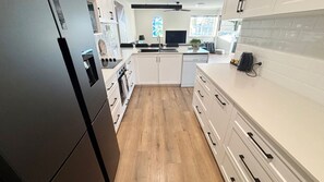A modern kitchen with white cabinetry, a black refrigerator, and a wooden floor. - Beach View Penthouse (SOUTH WEST ROCKS)
