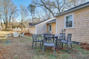 A house with a patio area featuring a table and chairs, surrounded by a lawn with scattered leaves. - Walk to Monument Beach: Cape Cod Cottage w/ Grill (Bourne)