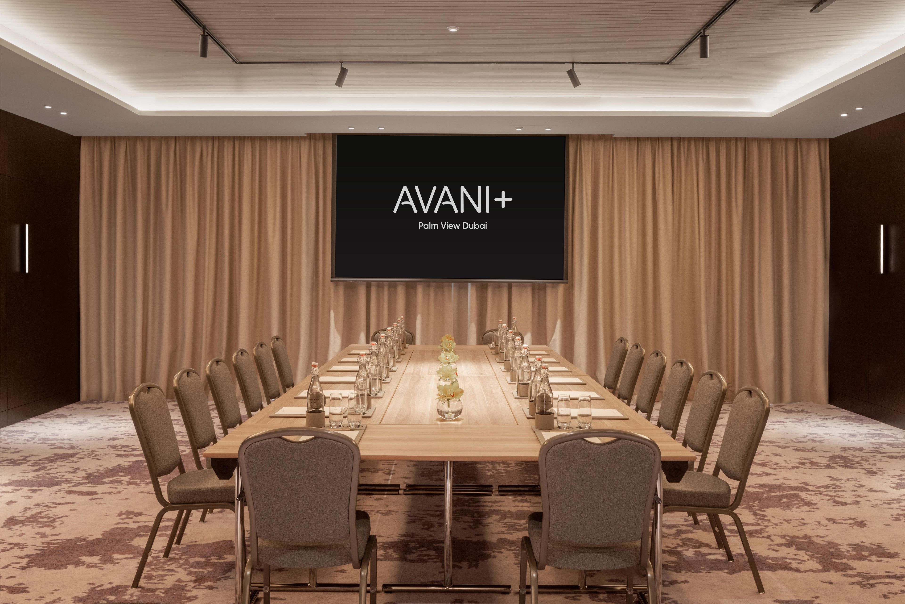 Une salle de conférence équipée d’une longue table, de chaises et d’un écran affichant la mention « AVANI+ Palm View Dubai ».