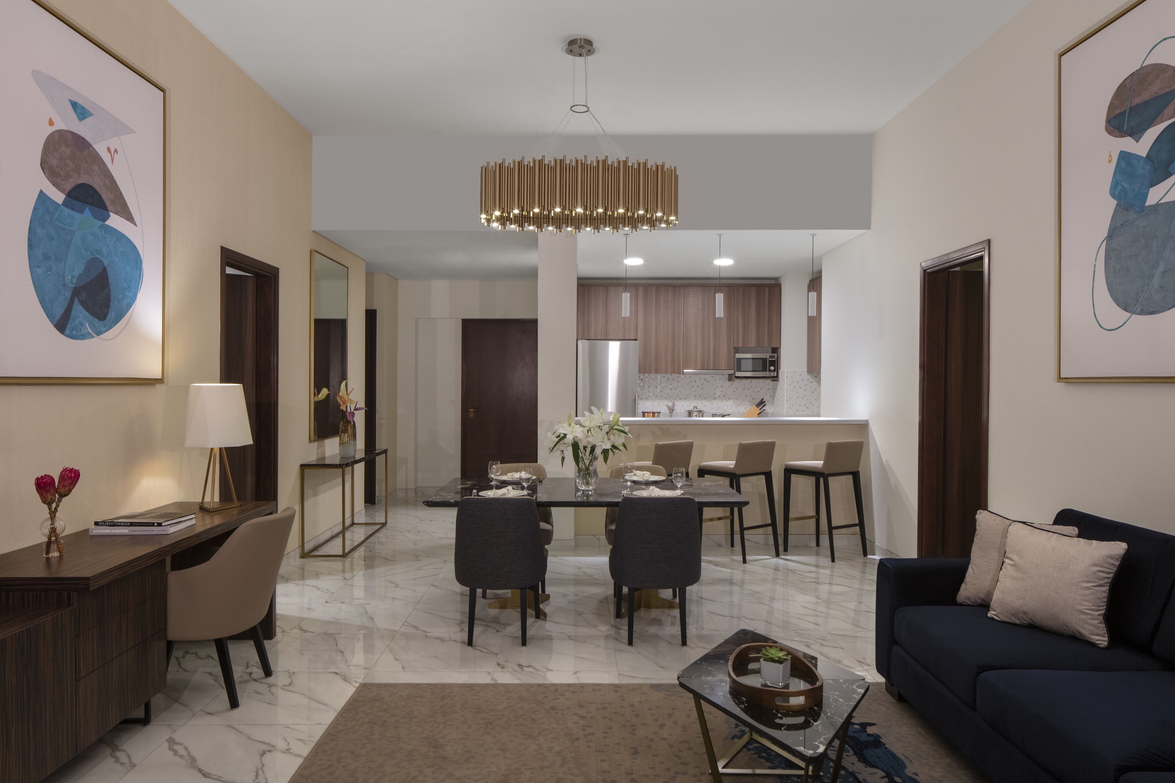 A modern living room with a dining area, kitchen in the background, and artwork on the walls.
