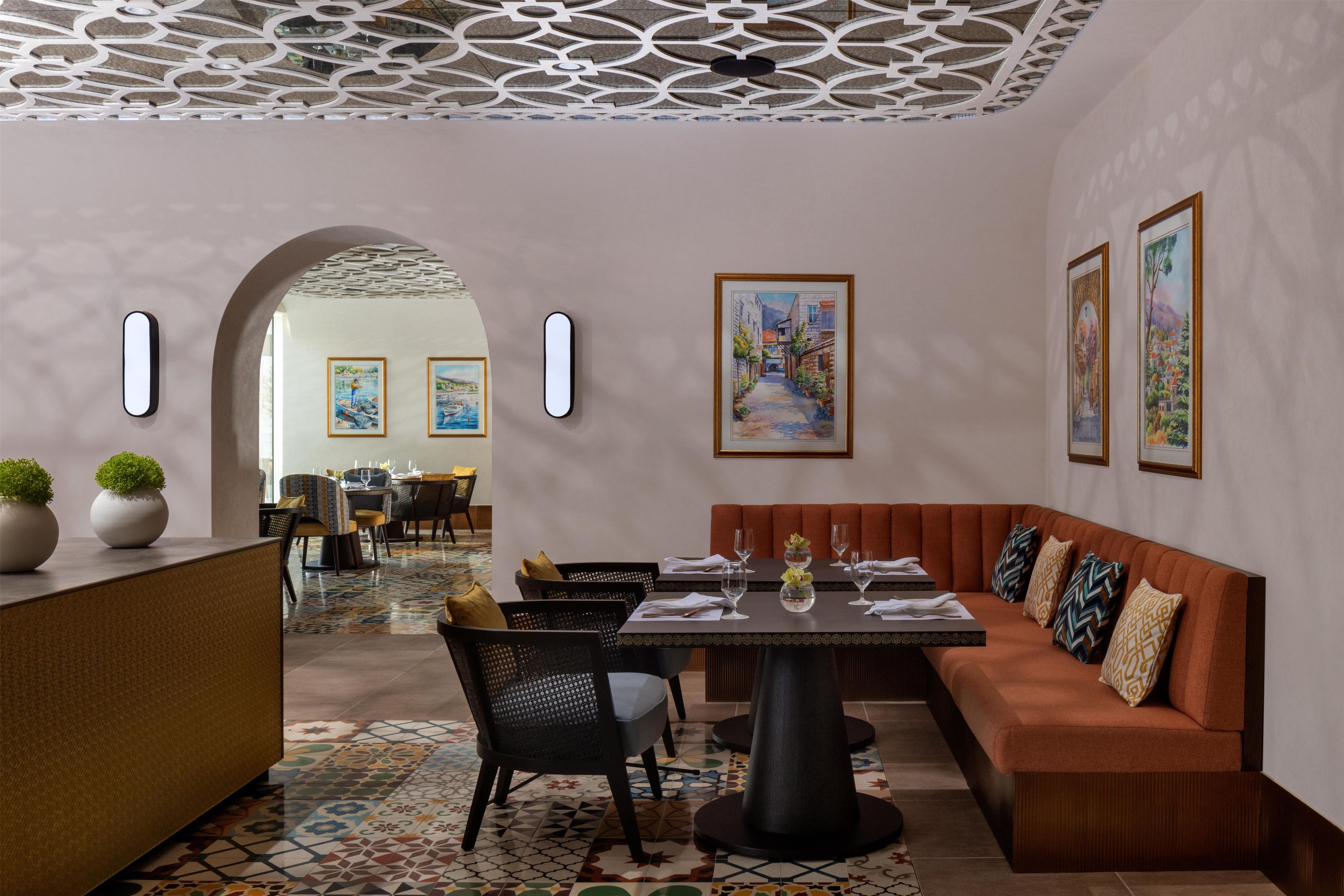 A dining area with a high ceiling, patterned floor, and a mix of seating options including a booth and a long table.