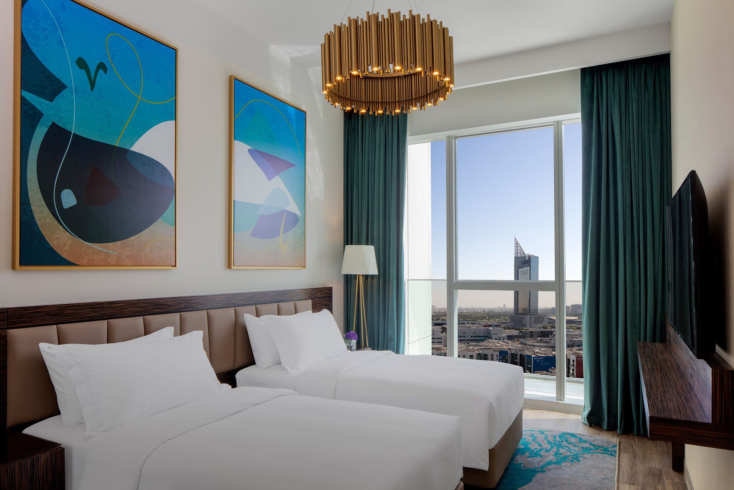 A hotel room with two beds, a large window with a city view, abstract art on the wall, and a modern chandelier.