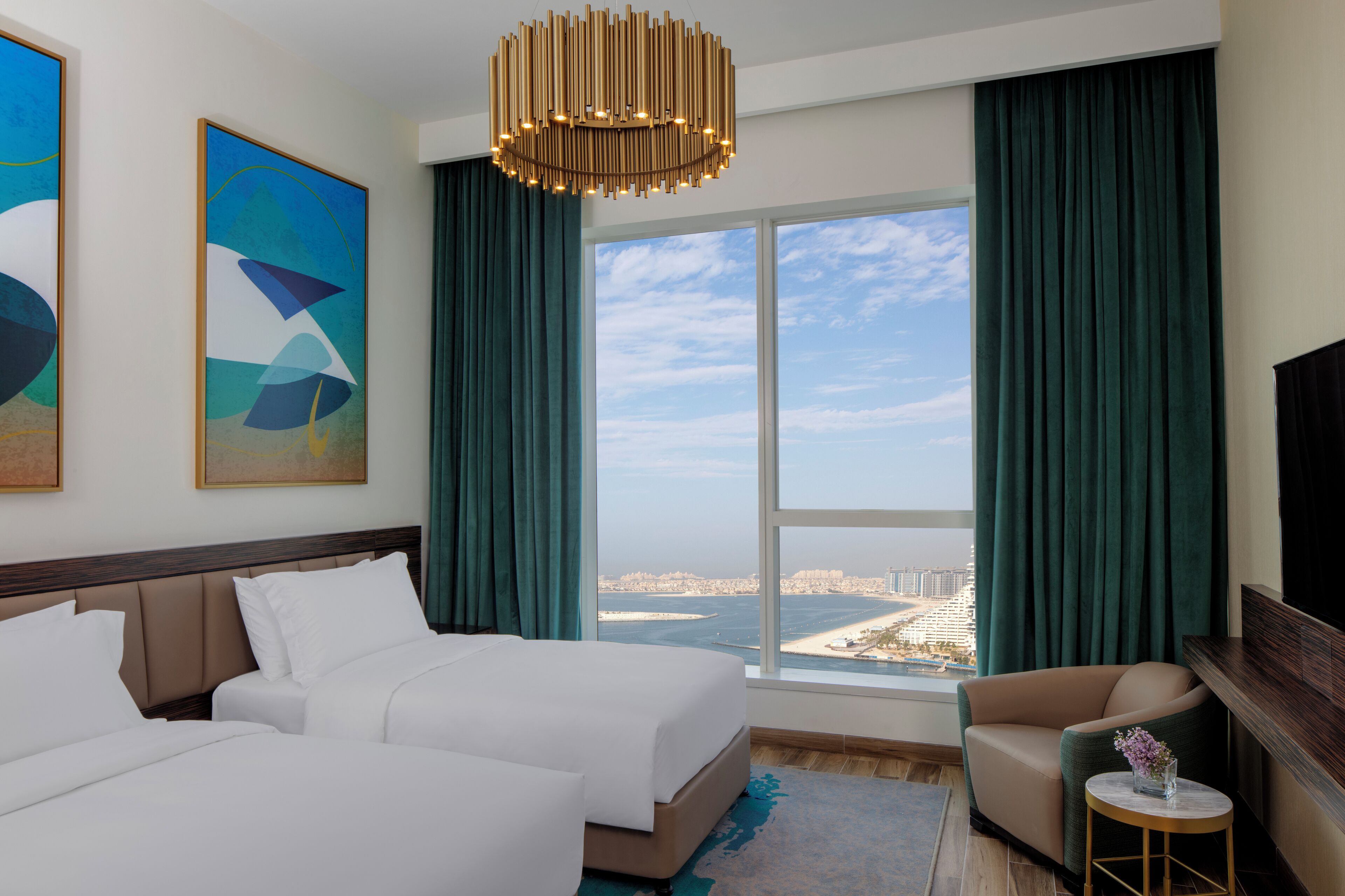 Ein Hotelzimmer mit einem großen Bett, einer Couch, einem kleinen Tisch und Blick auf Stadt und Meer.