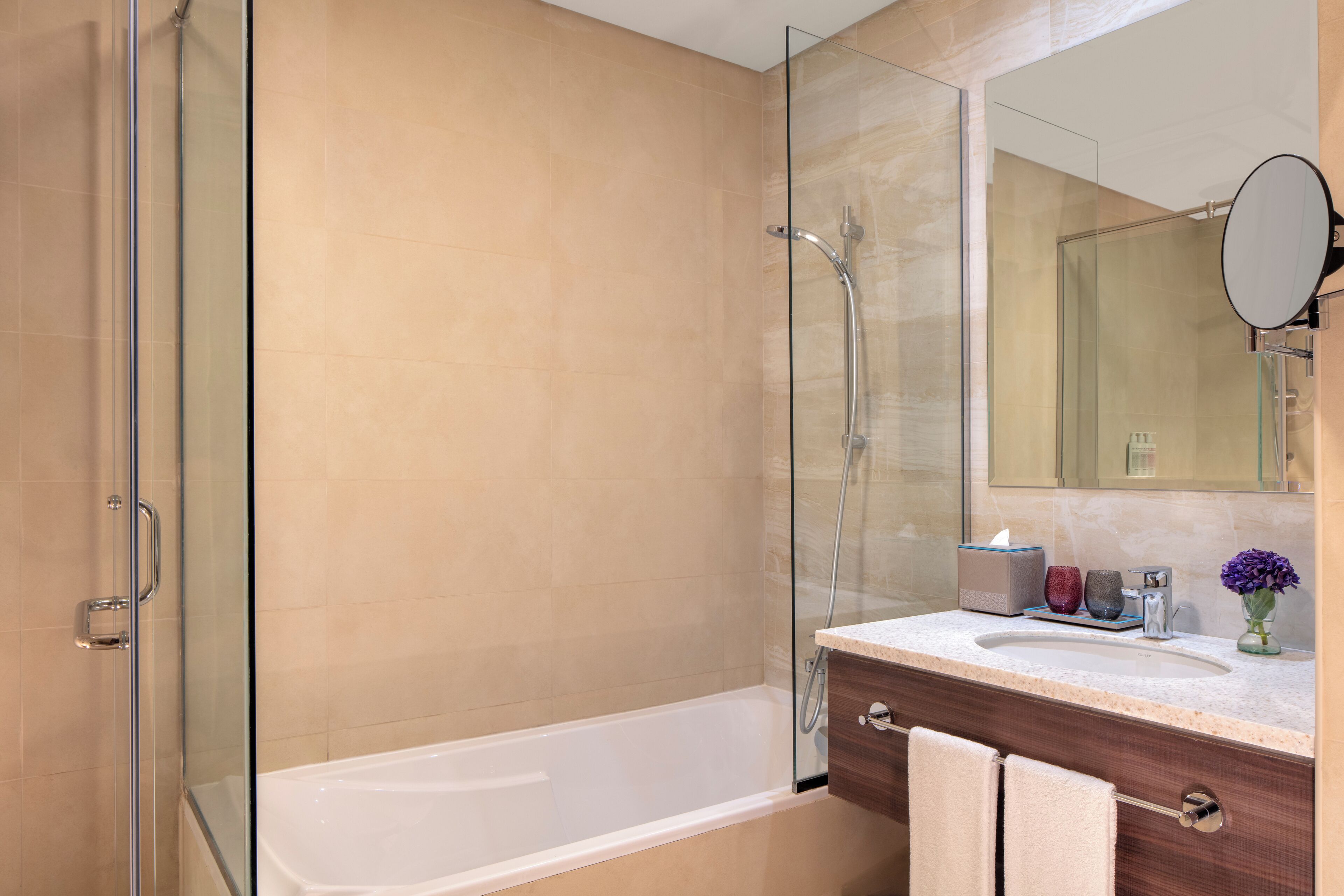 A modern bathroom with a glass-enclosed shower, a white bathtub, and a vanity with a mirror.