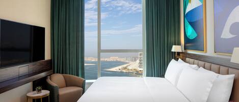 Una camera d'albergo con un letto grande, una televisione, una sedia, un tavolino e vista sulla città e sul mare.