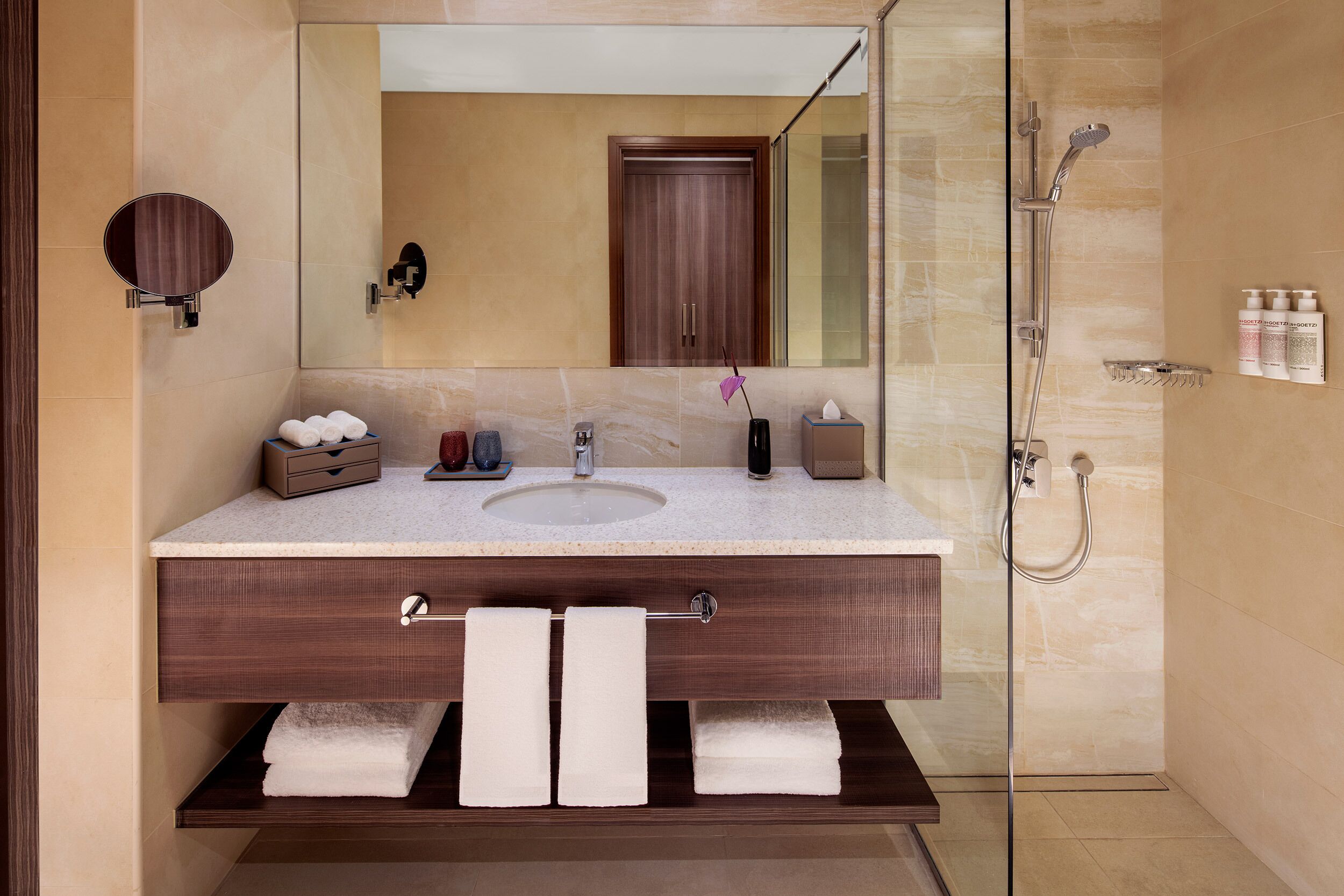 Un baño moderno con un espejo grande, un lavabo y una ducha. Hay toallas y artículos de aseo en el mueble.