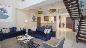 Amplia sala de estar con un amplio sofá, una mesa de centro y una mesa de comedor. Se ve una escalera que conduce a un nivel superior.