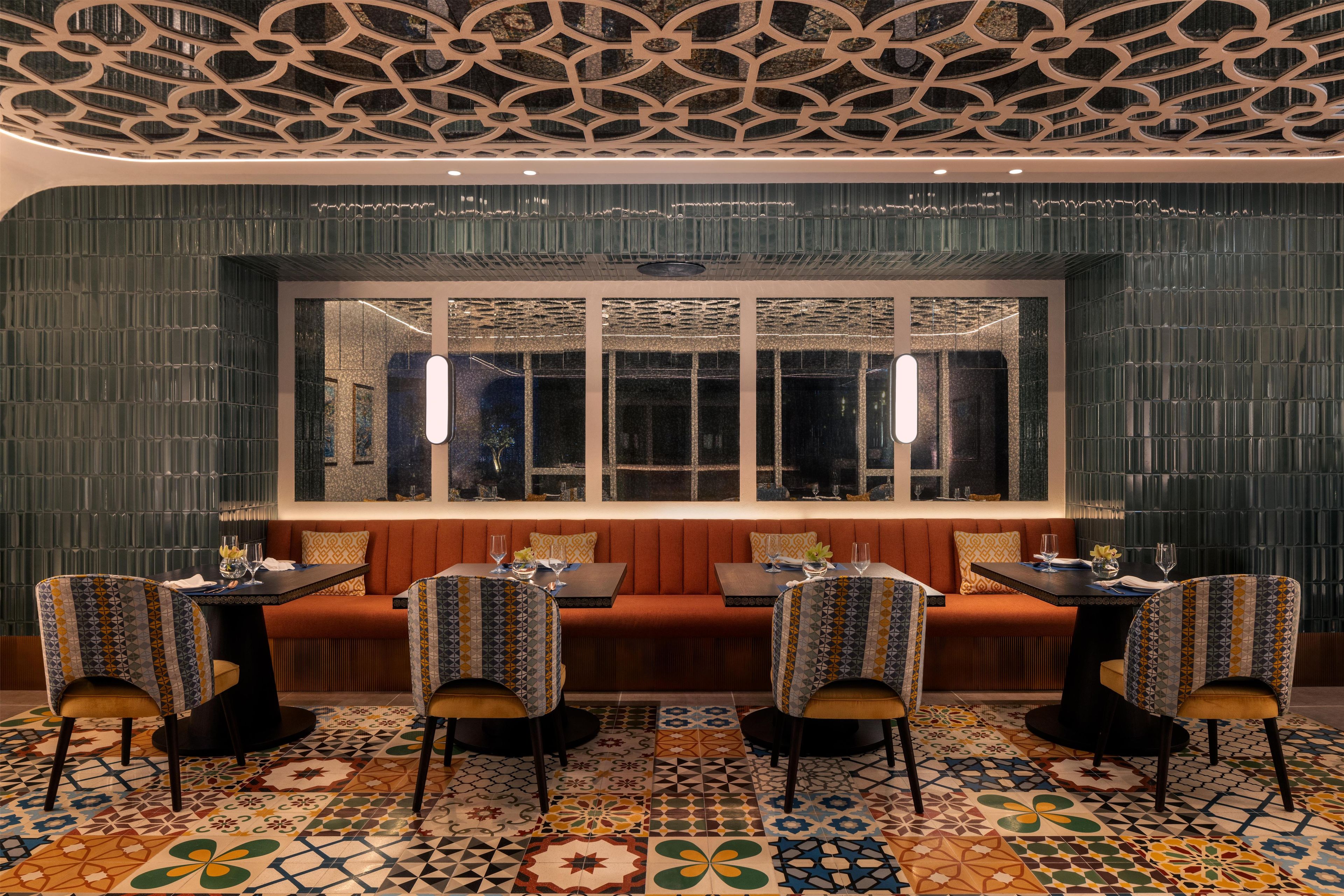 A restaurant interior with a patterned floor, a seating area with tables and chairs, and a decorative ceiling.