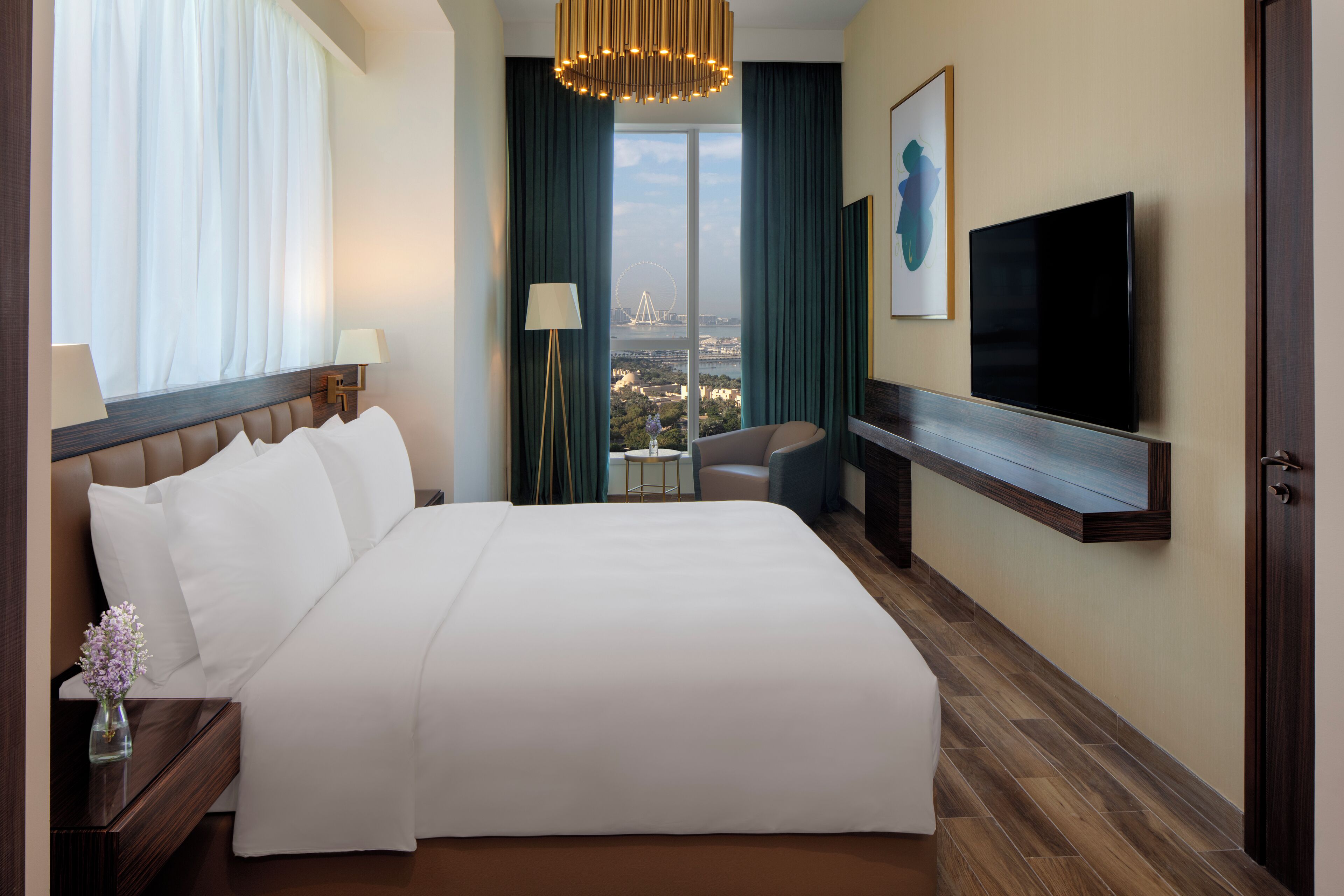 A hotel room with a large bed, a TV mounted on the wall, a view of a Ferris wheel, and a cityscape visible through the window.