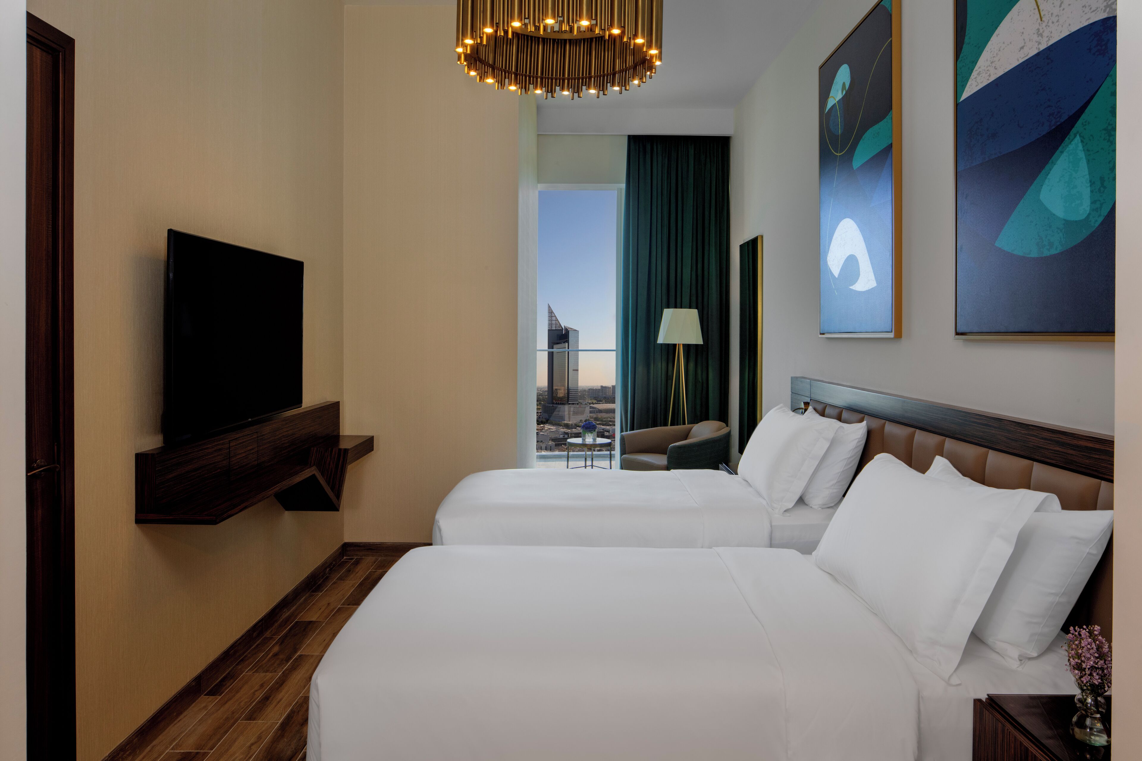 Een hotelkamer met twee bedden, een televisie aan de muur en een uitzicht op de stadsgezicht door het raam.