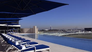 A poolside area with lounge chairs and umbrellas, a clear sky, and a distant cityscape.