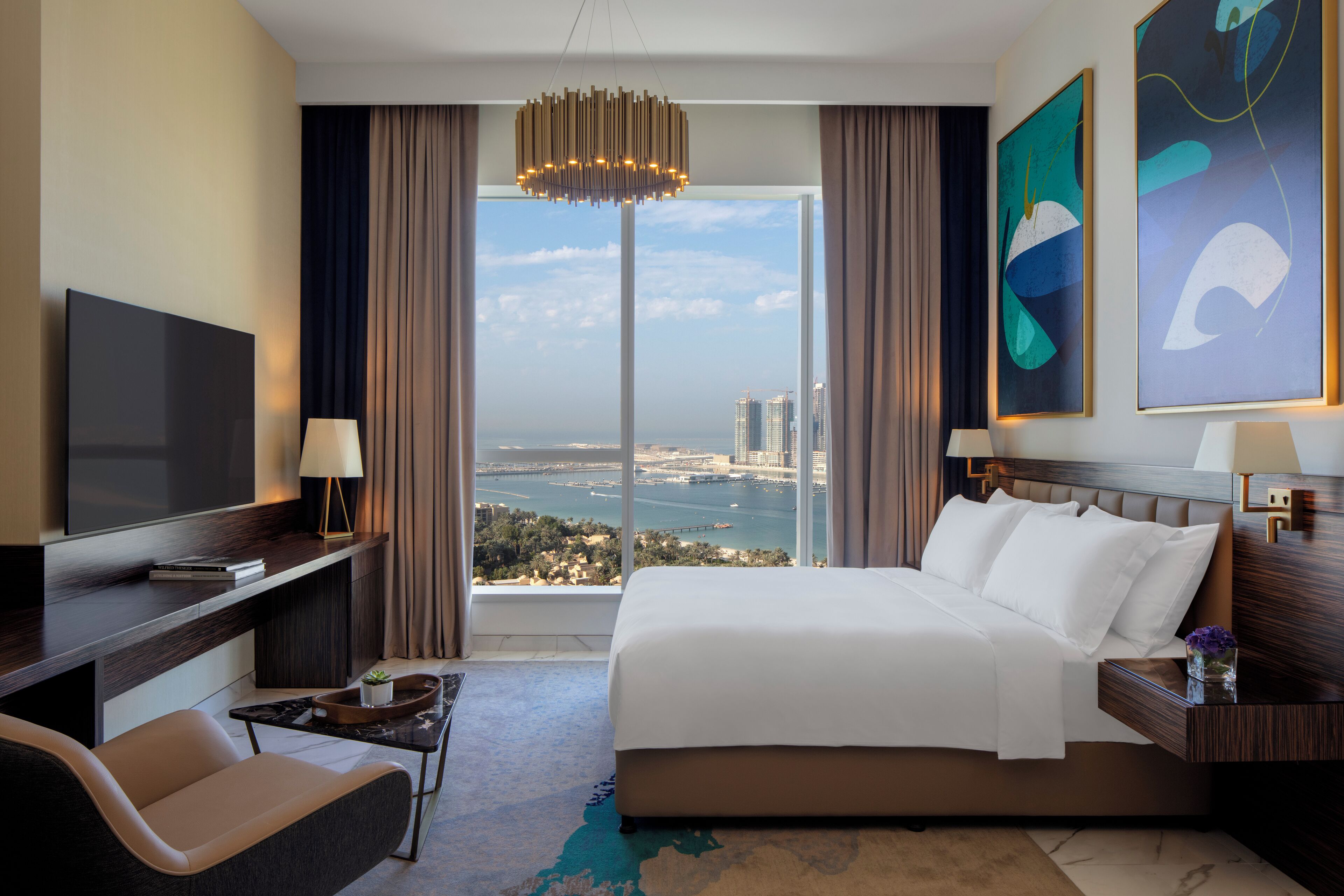 Habitación de hotel con una cama grande, televisión, escritorio y vista a la ciudad.