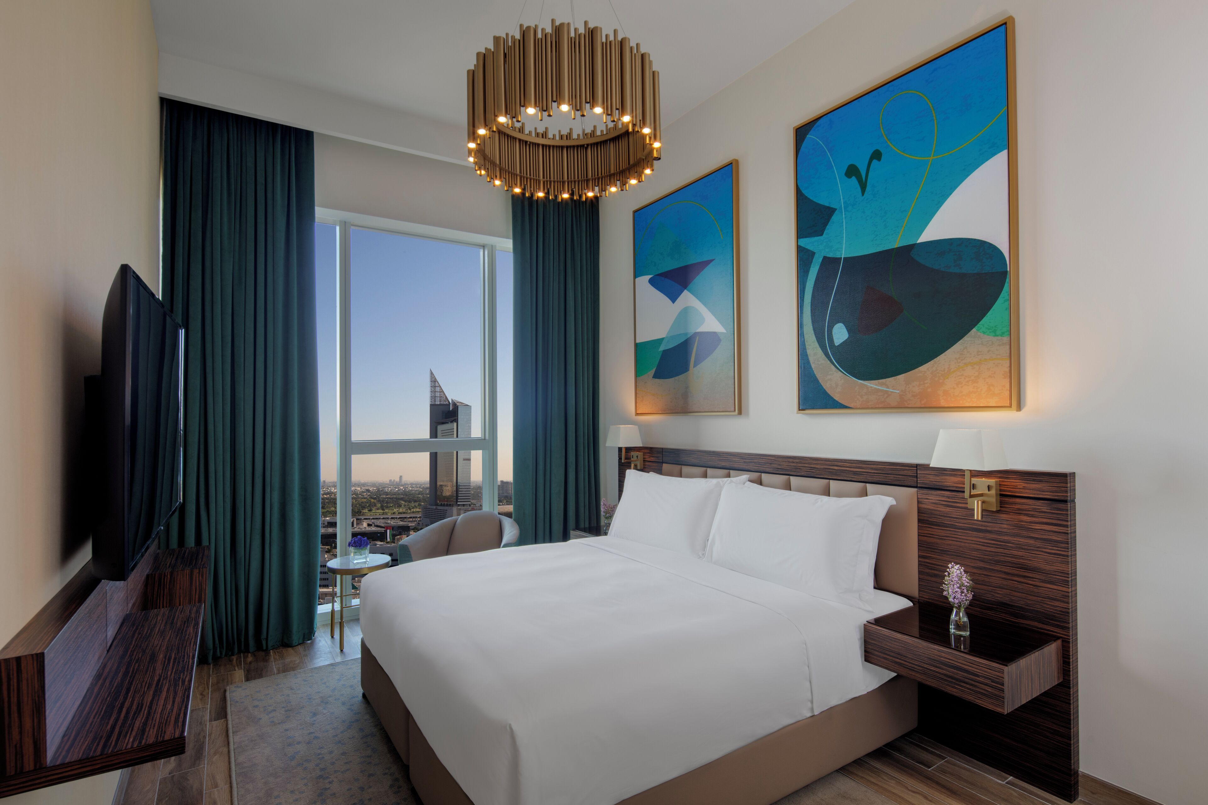 A hotel room with a large bed, a TV, a desk, and a view of the city.