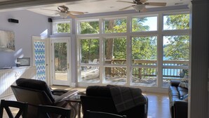Un salon spacieux doté de grandes fenêtres, d’un ventilateur de plafond et offrant une vue sur une terrasse et des arbres.
