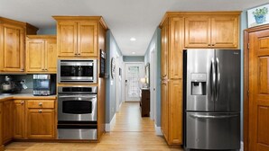 Une cuisine dotée de meubles en bois, d’appareils électroménagers en acier inoxydable et d’un couloir menant à une porte.