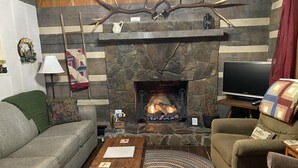 A cozy living room with a stone fireplace, a television, and comfortable seating.