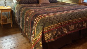 A log cabin bedroom with a large bed, two bedside lamps, and a window with blinds.