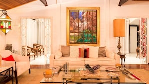 A cozy living room with a wooden ceiling, a large window with a forest scene, a sofa with cushions, a coffee table with decorative items, and a lamp. - Single room in a luxury hotel. (RJ)