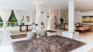 A spacious, modern living room with a large, fluffy rug, a dining area with a glass table, and a view of lush greenery outside. - Single room in a luxury hotel. (RJ)