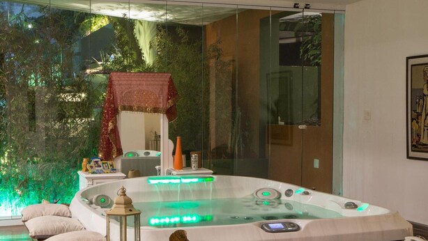 A modern spa room with a hot tub, a glass-enclosed shower, and a wooden bench with books. - Single room in a luxury hotel. (RJ)