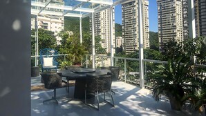 A glass-enclosed balcony with a table and chairs, overlooking tall residential buildings and greenery. - Single room in a luxury hotel. (RJ)