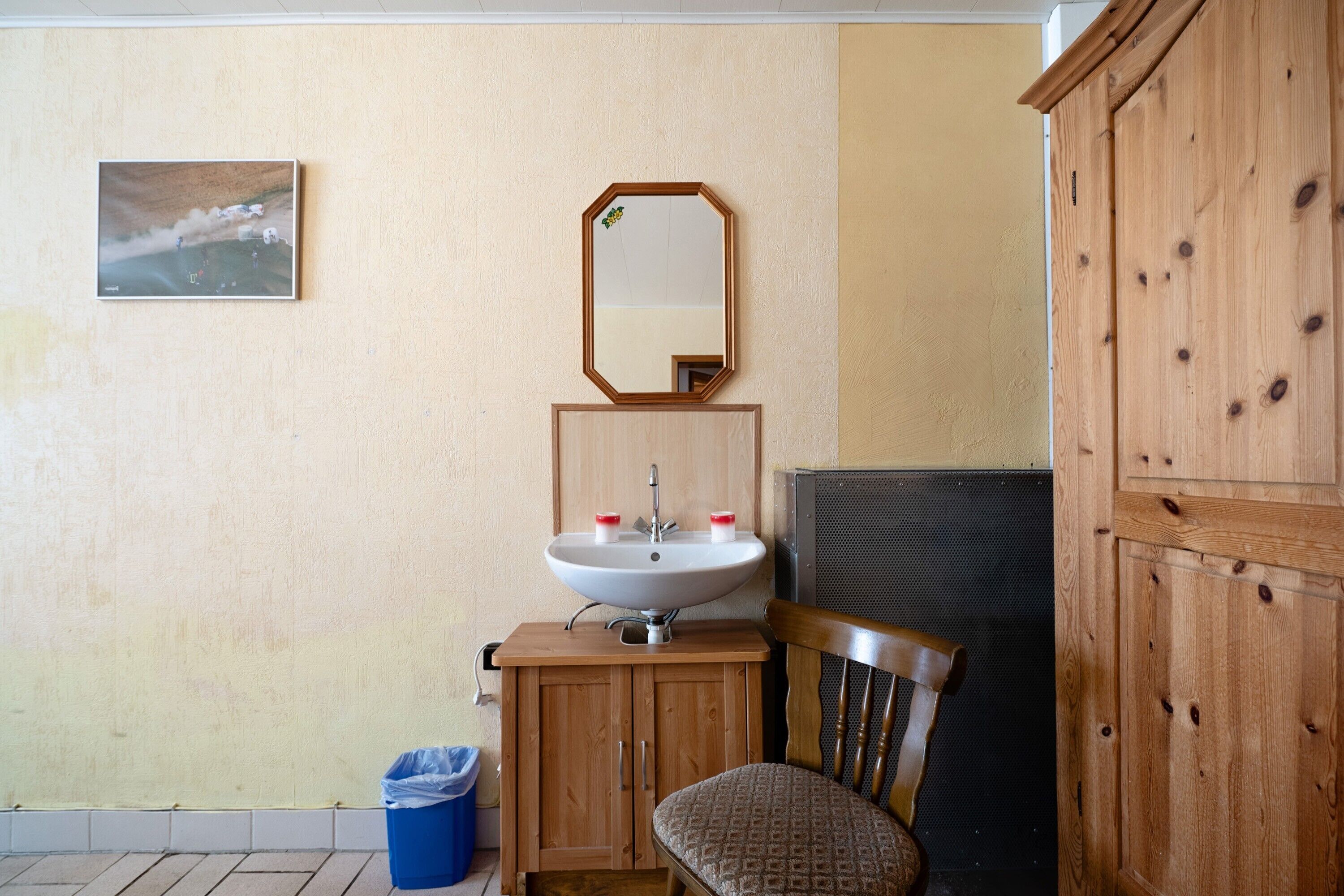 Une salle de bain équipée d’un lavabo, d’un miroir, d’un meuble en bois, d’une chaise et d’une poubelle.
