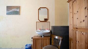 Une salle de bain équipée d’un lavabo, d’un miroir, d’un meuble en bois, d’une chaise et d’une poubelle.