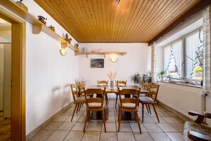 Un coin repas avec une table et des chaises en bois, un sol carrelé et une fenêtre avec des rideaux.