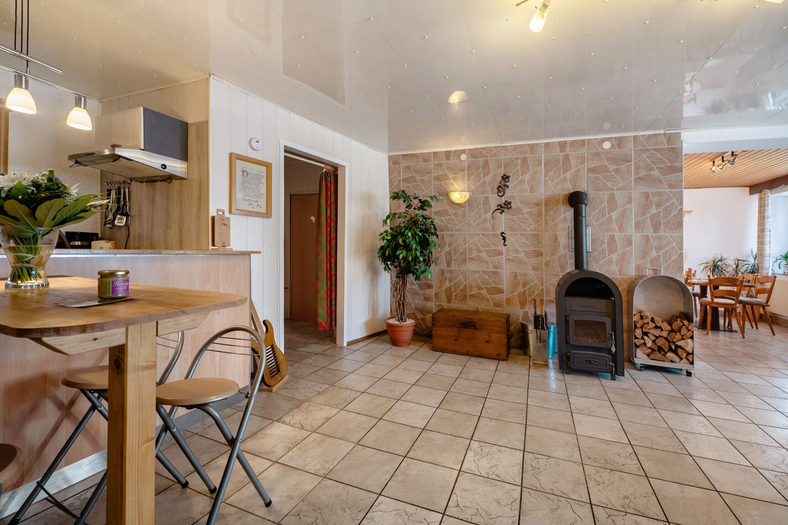 A spacious kitchen with a stone wall, a wood-burning stove, and a dining area with chairs and a table.