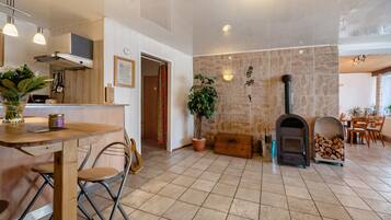 A spacious kitchen with a stone wall, a wood-burning stove, and a dining area with chairs and a table.