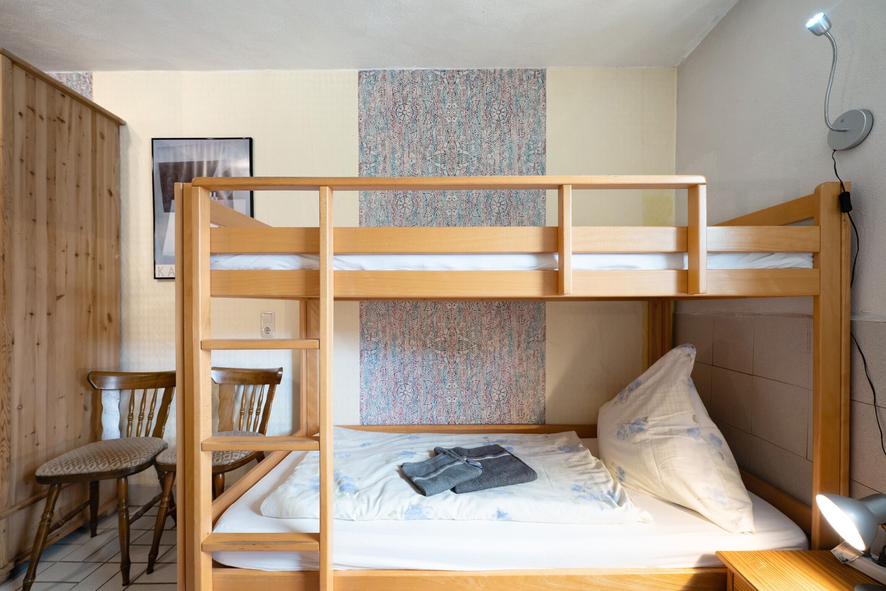 Un letto a castello con struttura in legno, una scrivania, una sedia e una lampada fissata al muro.