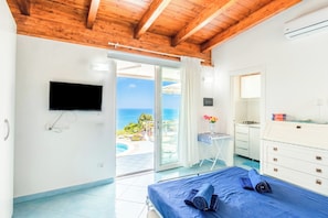 A bedroom with a bed, a TV, a desk, and a view of the ocean.