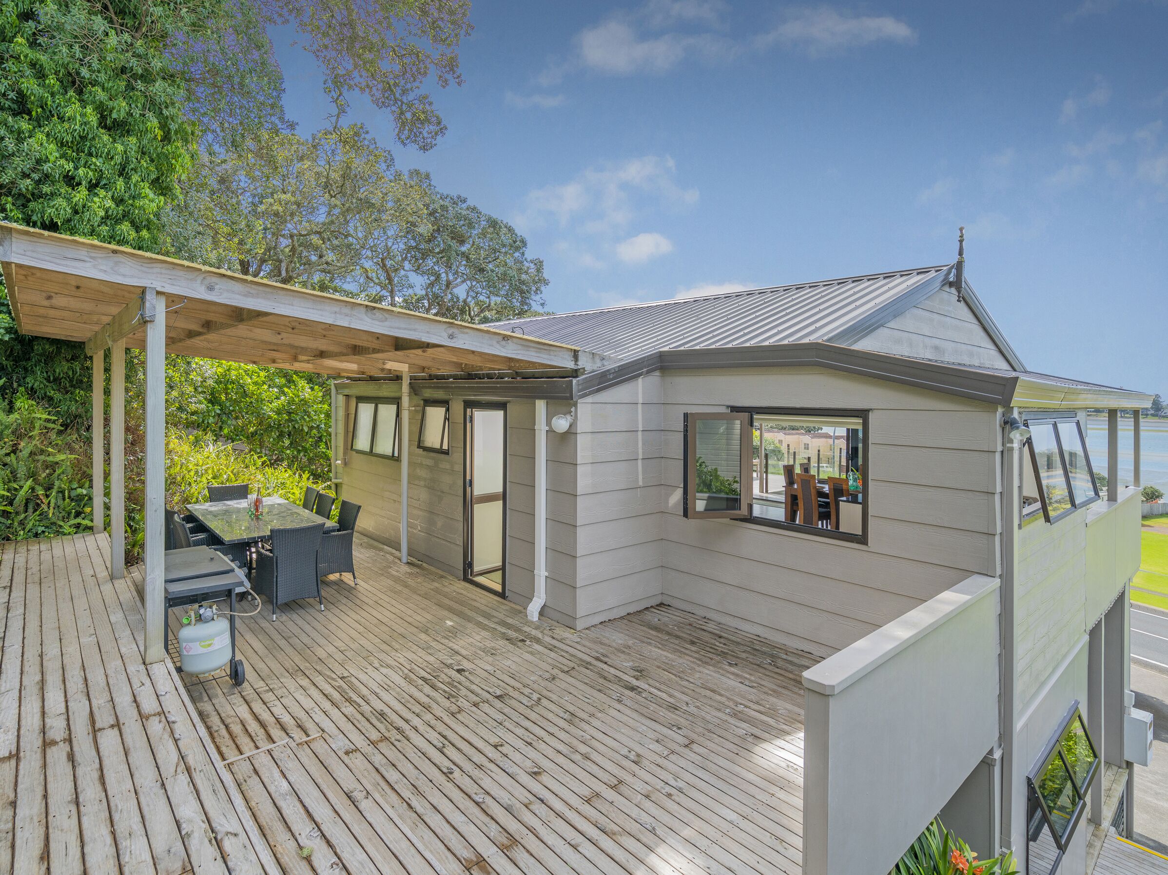 A covered outdoor area with a wooden deck, a small building with a window, and a view of a green landscape.