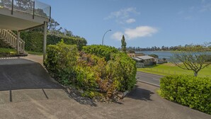 A parking area with a covered walkway leading to a building, surrounded by greenery and a view of a body of water.