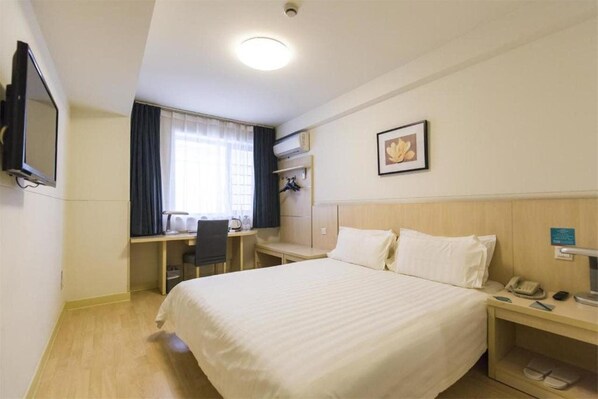A hotel room with a bed, desk, chair, and a television.
