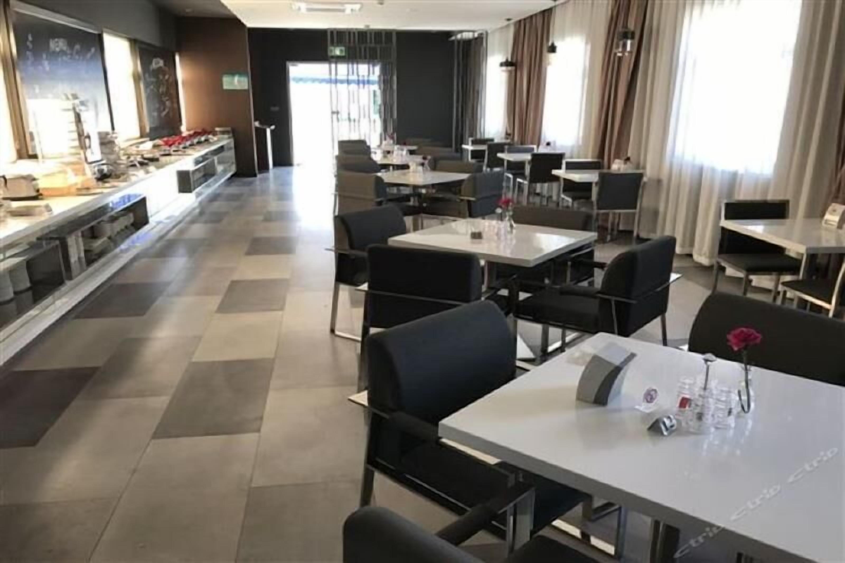 Un'area ristorazione di un hotel moderno con un lungo bancone, diversi tavoli e sedie.