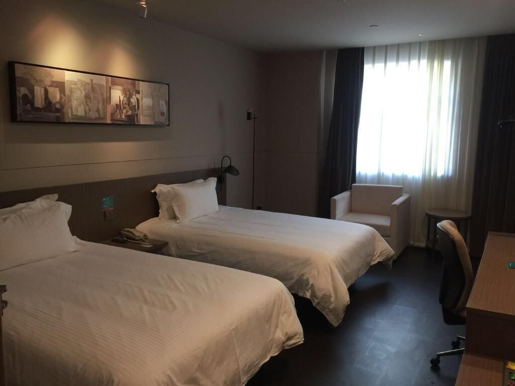 A hotel room with two beds, a desk, a chair, and a large window with curtains.