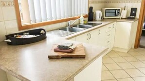 A kitchen with a sink, a microwave, and a cutting board with a knife on the counter. - Rye Sleeps 10, Great Weekender (Rye)