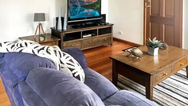 A living room with a sofa, a wooden coffee table, a TV on a wooden stand, and a door in the background. - Rye Sleeps 10, Great Weekender (Rye)