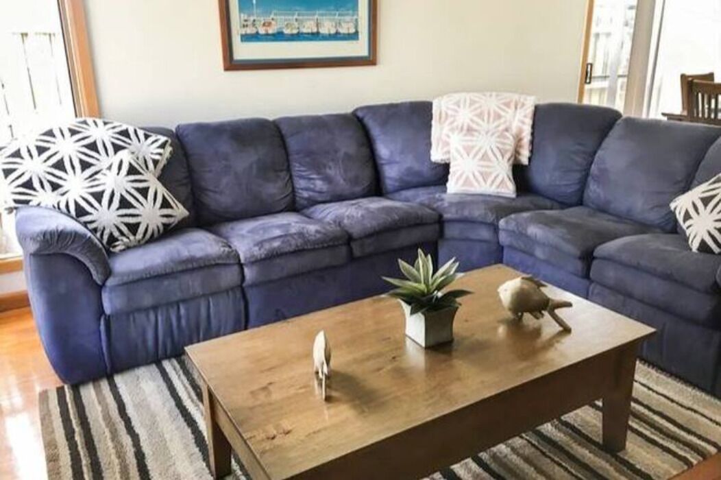 Een woonkamer met een donkerblauwe modulaire bank, een houten salontafel en een gestreept tapijt.