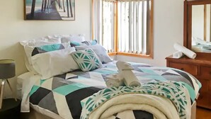 A neatly made bed with a geometric patterned bedspread, a bedside lamp, and a window with vertical blinds. - Rye Sleeps 10, Great Weekender (Rye)